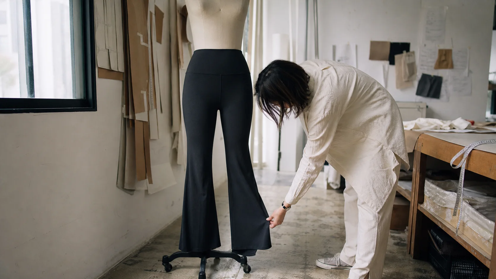 Tailor checking the hem fall of black flare yoga pants on a dress form