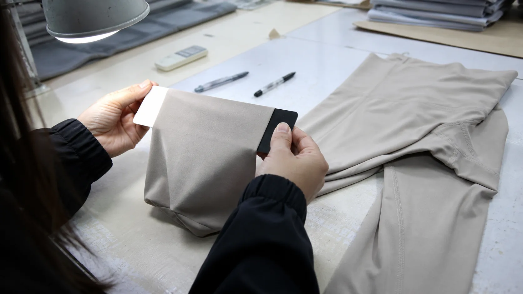 Quality technician stretching pale yoga fabric over black and white backing cards under an inspection lamp
