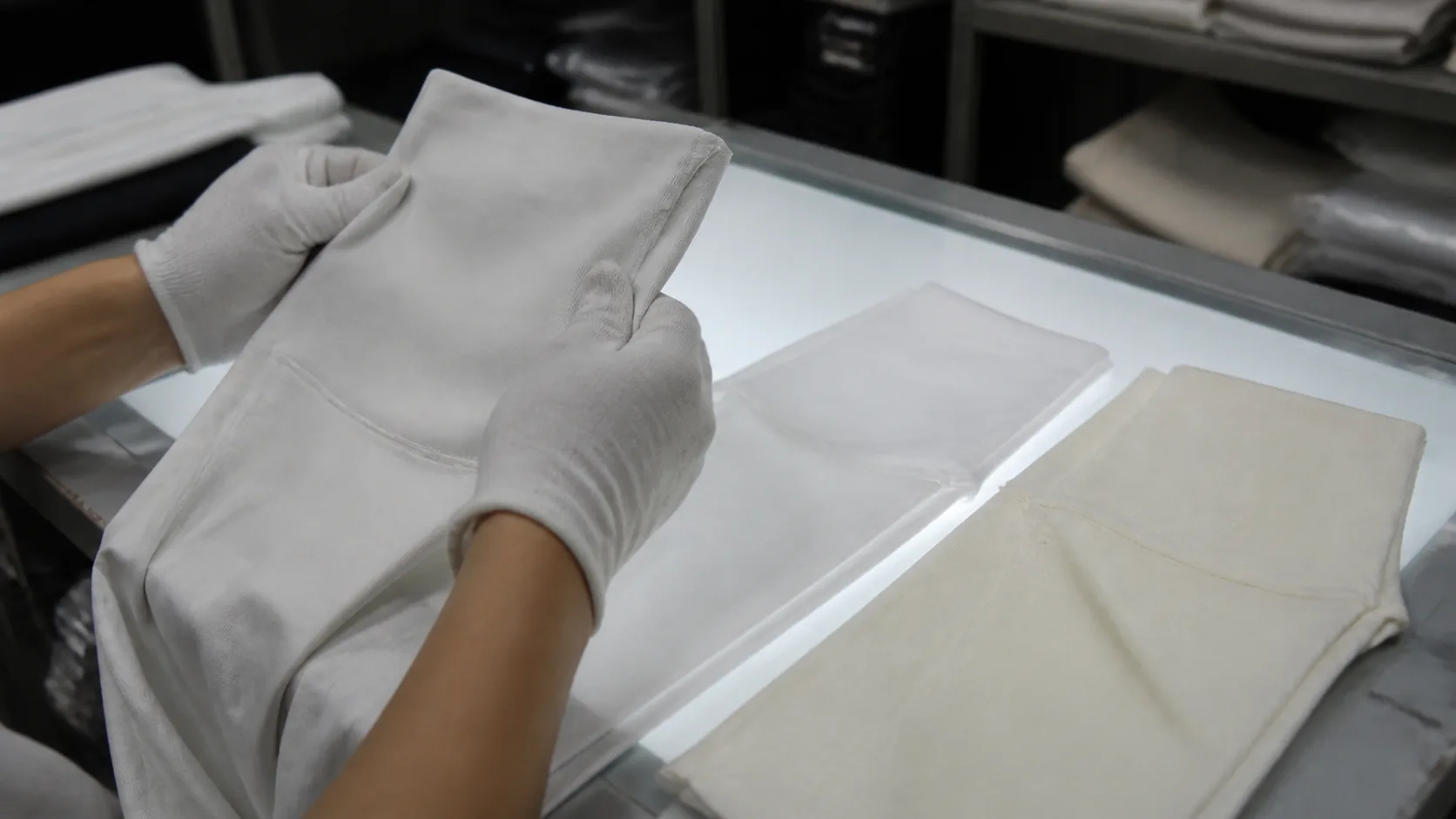 Gloved quality worker comparing clean white and slightly yellowed yoga fabric panels over a light table