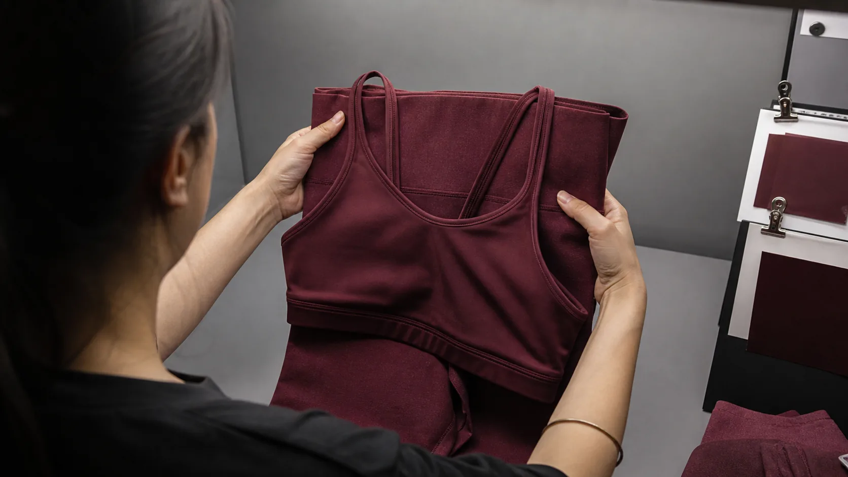 Color technician comparing burgundy yoga bra and legging fabrics together in a viewing booth