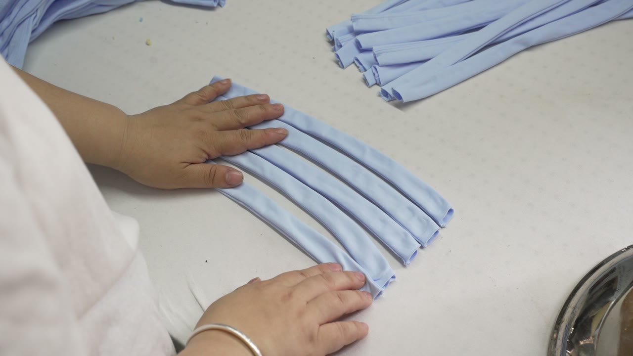 Hands smoothing light-blue fabric strips on a pressing table