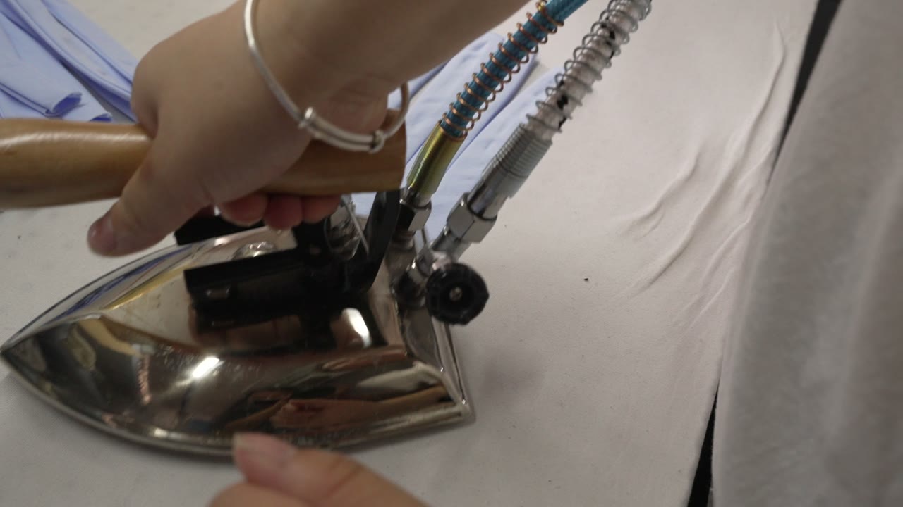 Hand-held steam iron pressing light-blue fabric strips